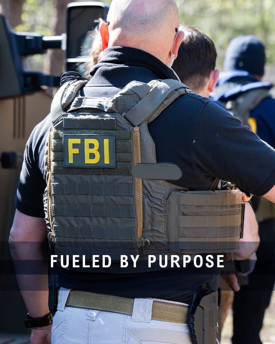 FBI agent in tactical vest outdoors, back view with yellow FBI patch; official FBIJobs recruiting still (“Fueled by purpose”)