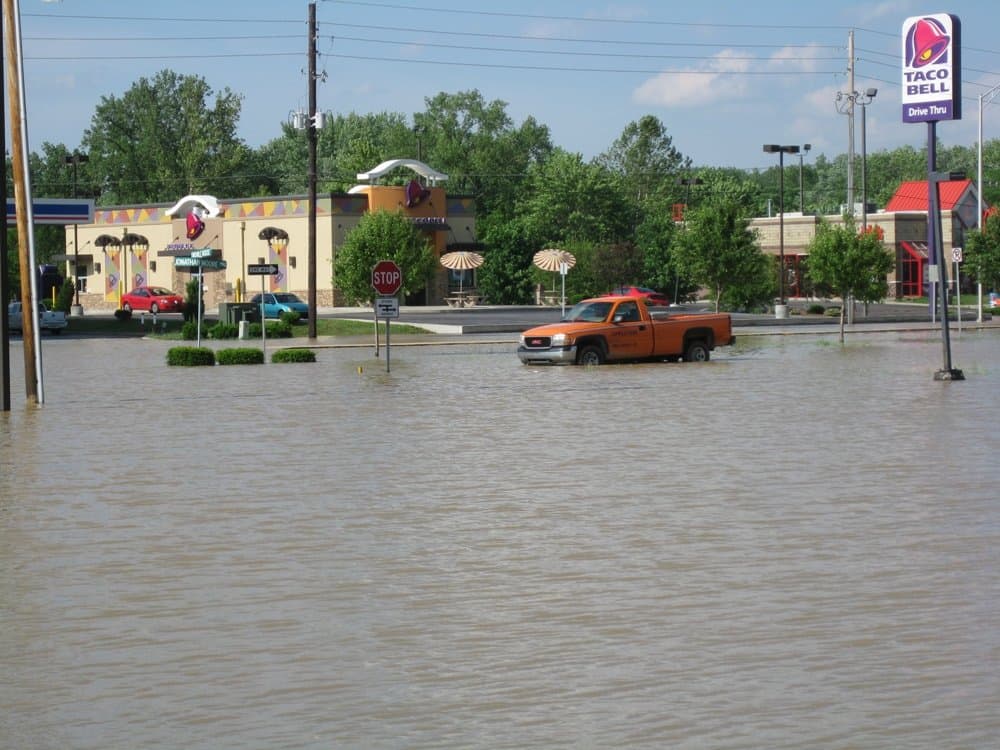 An orange pickup truck sits in muddy floodwater in a commercial parking lot beside a Taco Bell in Columbus, Indiana; street signs poke above the water. File photo, June 8, 2008.