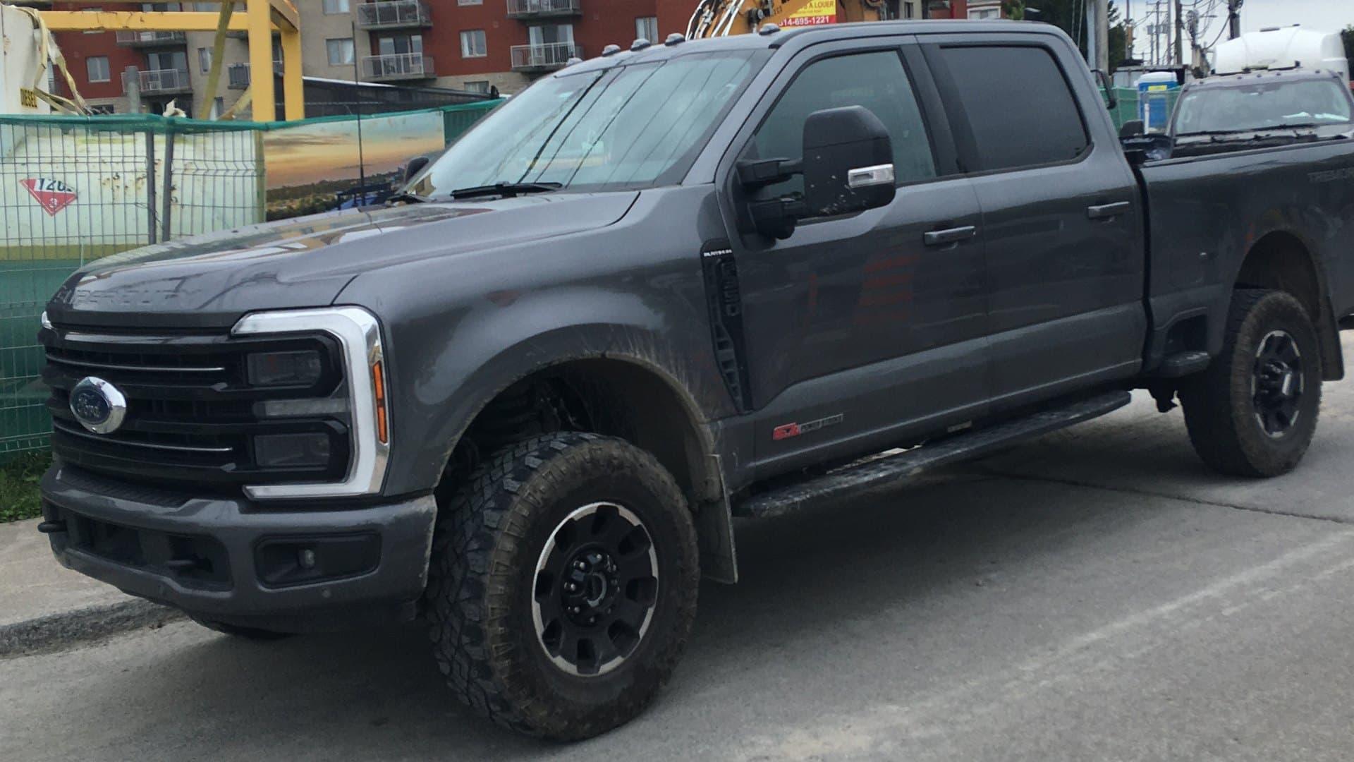Dark gray Ford F-350 Super Duty Crew Cab pickup with off-road tires parked on a street, seen from the front left