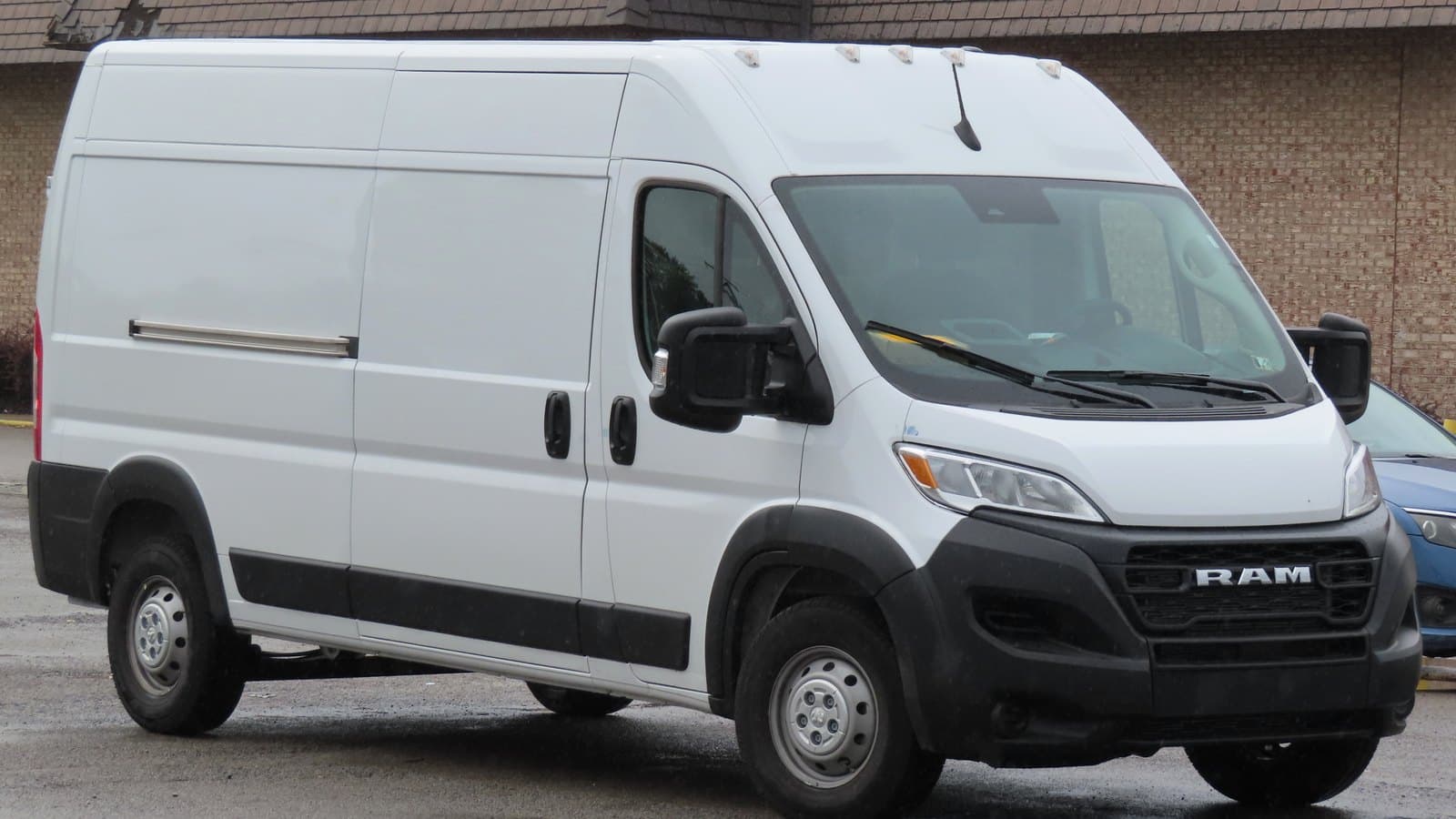 White 2023 Ram ProMaster 2500 high-roof cargo van parked on a wet lot, seen from the front right